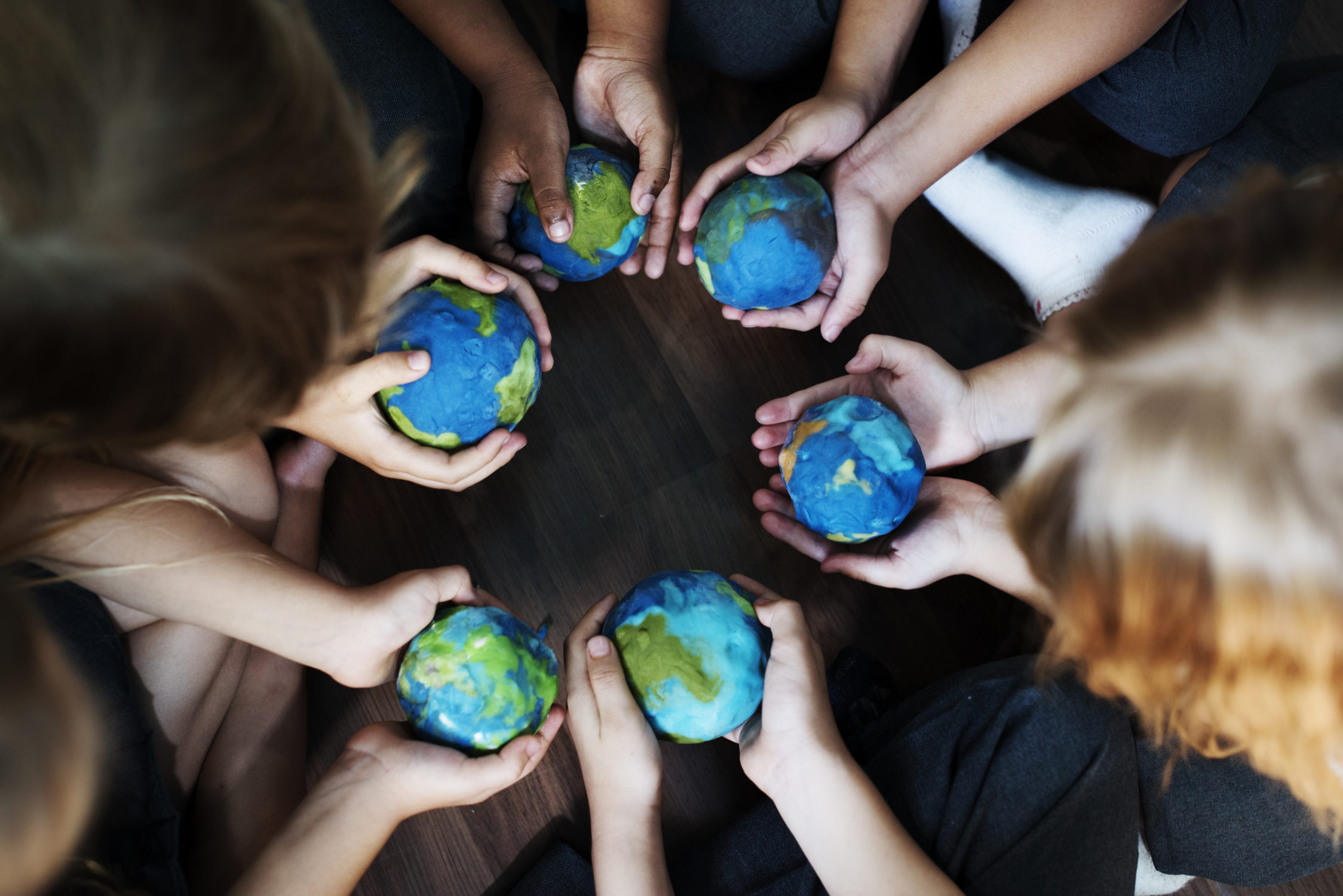 Group of diverse kids hands holding cupping globe balls together